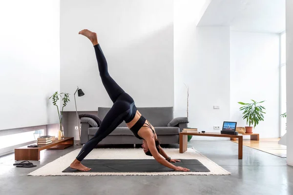 Bir bacağı aşağıya doğru bakan bir kadın evdeki yoga eğitim programını kullanarak köpeğe doğru gidiyor.