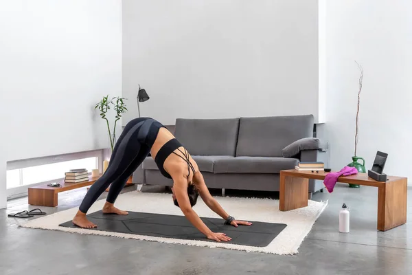 Kadın, evdeki tabletteki yoga programını kullanarak köpeğe doğru eğiliyor.