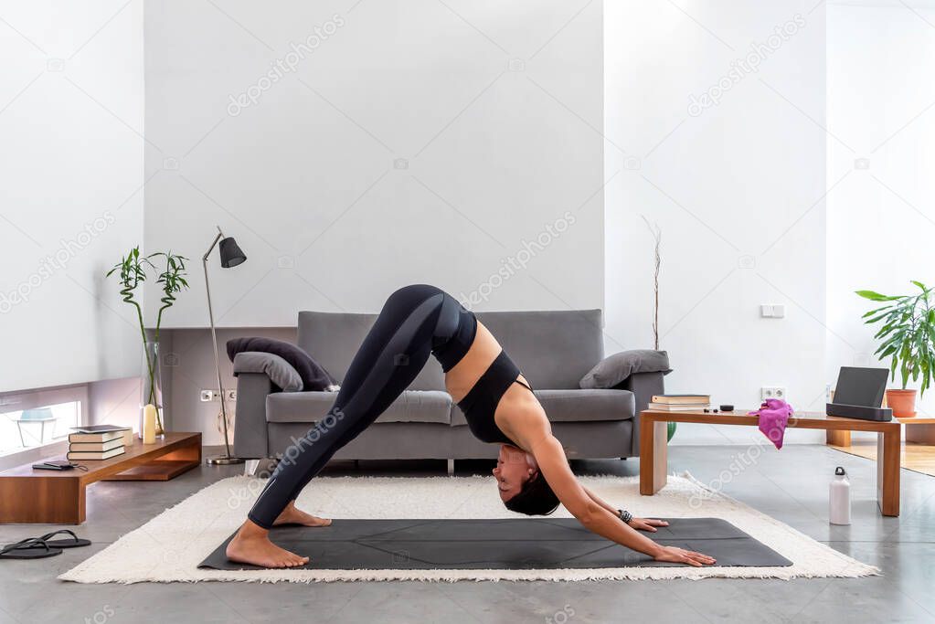 Woman doing downward facing dog using online yoga training program in the tablet at hom