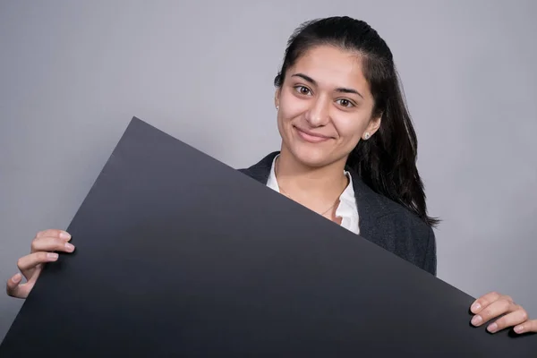 Retrato de uma bela mulher de negócios indiana em um terno de negócios, segurando um fundo preto em sua mão, um branco. Espaço livre. Fotografia de estúdio. Num fundo cinzento. Conceito de negócio — Fotografia de Stock