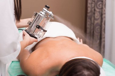 Profesyonel bir kozmetik uzmanı genç bir hastanın sırtına gerekli yağı püskürten bir cihaz kullanıyor. Güzellik salonunda spa tedavisi