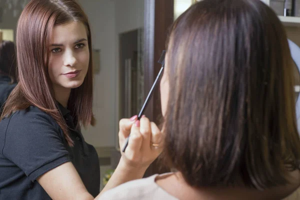 Porträtt av en ung vacker makeup artist flicka. Makeup mästare gör makeup till en flicka. — Stockfoto