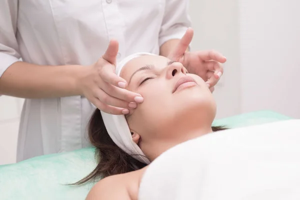 A massagista faz massagens faciais com uma mulher bonita. As mãos estão a fechar. Sala de massagem — Fotografia de Stock