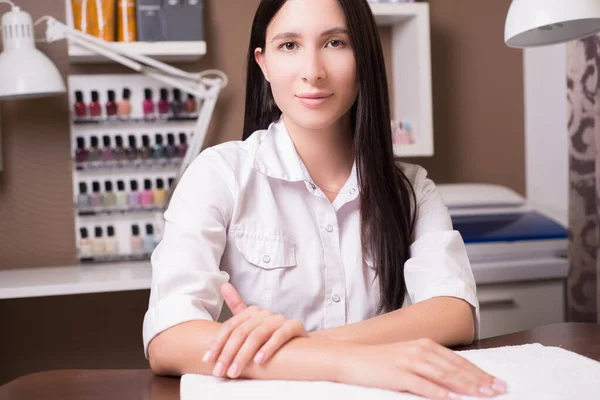 一个25岁的年轻漂亮姑娘的画像，穿着一件白衬衫，坐在桌旁，摆出优雅的姿势。 在美容院卖化妆品的女售货员. 美容师 — 图库照片