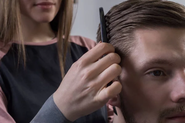 close-up master hairdresser doing hair styling so that the bearded guy combed his hair with a comb