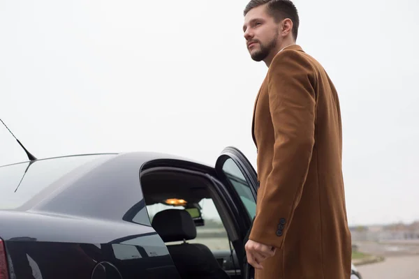 Retrato de un joven en ropa de negocios, un hombre de negocios de treinta años abre la puerta del coche para salir. En una interesante autoría —  Fotos de Stock