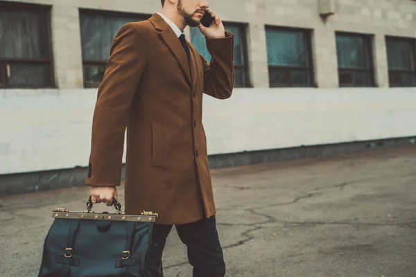 Portret van een jonge zakenman van dertig, in een zakelijke stijl, een man in een pak, vastgebonden met een leren tas in zijn handen. Een jonge man op straat, staat tegen de achtergrond van een kantoorgebouw — Stockfoto