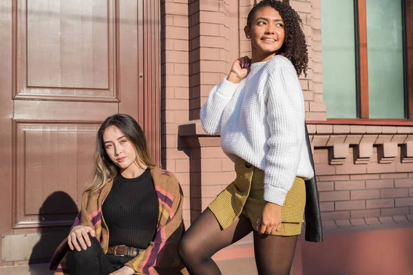 A pair of beautiful young fashionable Spanish girls, against the background of a brick office building. Posing for the camera. Generation Z — Stock Photo, Image