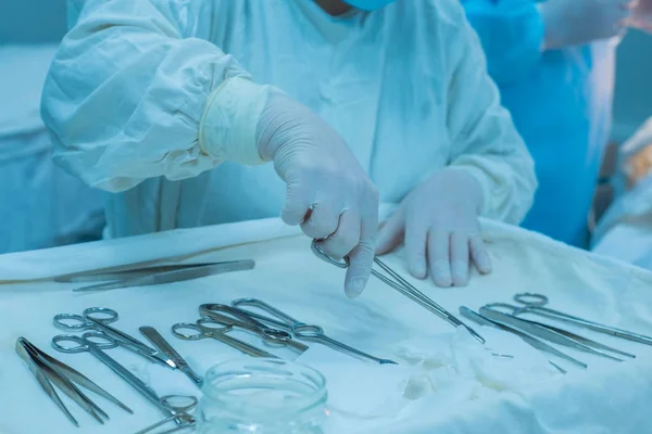 手術を行う医師のチームを背景に滅菌テーブルから医療機器を採取する外科看護師の手が近くにあり — ストック写真