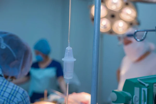 Ameliyathanedeki damlatıcının yakın plan görüntüsü. Çocuk cerrahlarından oluşan bir ekibin arka planına karşı, ameliyathanede çalışırlar.