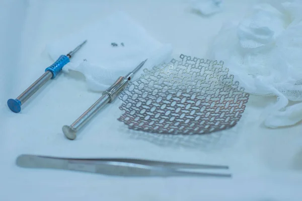 Close-up de uma mesa de operação estéril com instrumentos neurocirúrgicos médicos, incluindo uma placa de titânio, uma malha para o crânio, chaves de fenda médicas com parafusos . — Fotografia de Stock