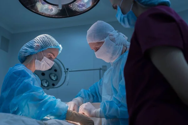 I chirurghi pediatrici eseguono chirurgia urologica. Un uomo e una donna in maschera, e un abito blu sterile, in sala operatoria. vista dal basso — Foto Stock