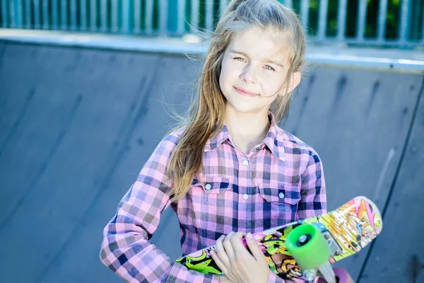 Bonito menina segurando um skate multicolorido — Fotografia de Stock