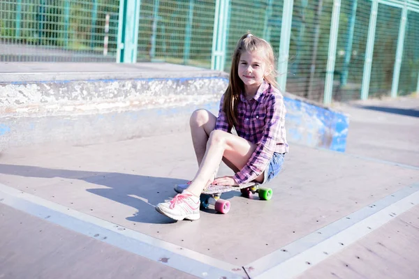Genç kız kaykayda oturuyor, açık havada kaykay parkında. — Stok fotoğraf