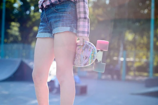 Adolescente sostiene en las manos el color del monopatín, en un hermoso sol — Foto de Stock