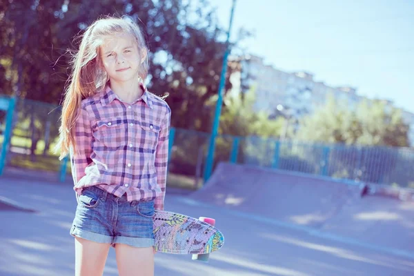 Retrato de uma adolescente, de pé em um parque de skate, segurando um skate na mão — Fotografia de Stock