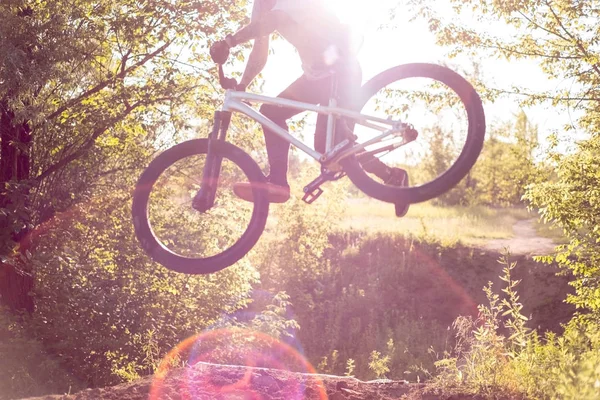 Mladík atlet, trénink dělá skoky a bike kaskadérské kousky v lese, proti zapadajícímu slunci. aktivní životní styl — Stock fotografie