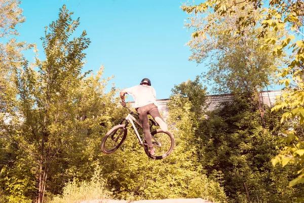 En ung kille, en idrottsman, utför tricks med en cykel, hoppar på språngbrädet. i skogen. mot solnedgången — Stockfoto