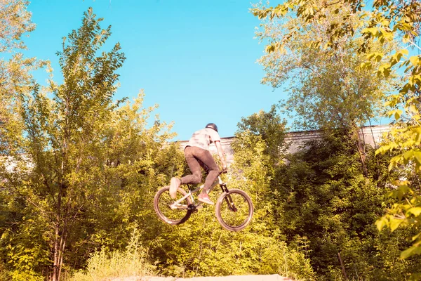En ung kille, en idrottsman, utför tricks med en cykel, hoppar på språngbrädet. i skogen. mot solnedgången — Stockfoto