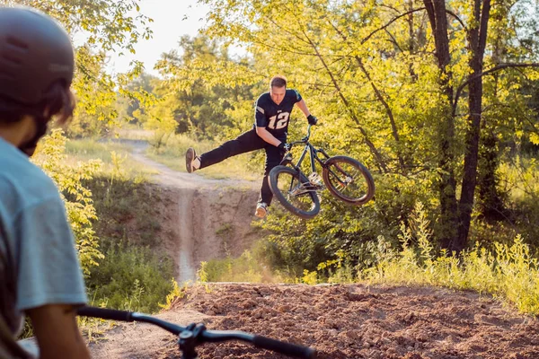 Cyklist - en vän ser ut som ung kille gör hopp och cykel stunts. i skogen mot solnedgången — Stockfoto