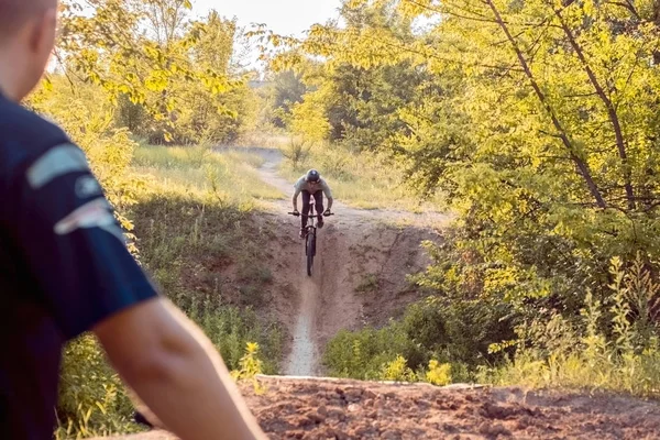 Ciclista assistindo seu parceiro andar de bicicleta. na floresta contra o pôr do sol — Fotografia de Stock