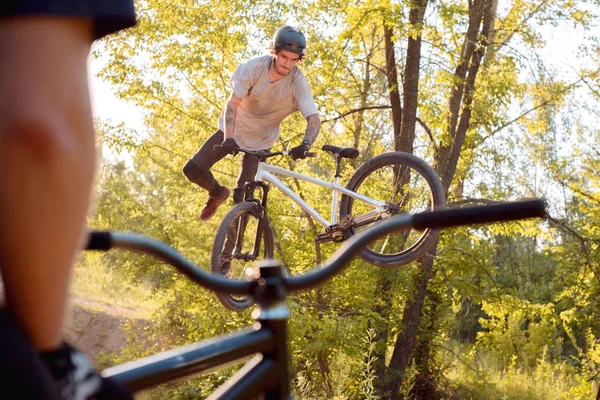 Młody facet z tatuażami, rowerzysta, skacze i wykonuje sztuczki na rowerze. widok przez ramę rowerową. w lesie przeciwko zachodzącemu słońcu. aktywny tryb życia — Zdjęcie stockowe