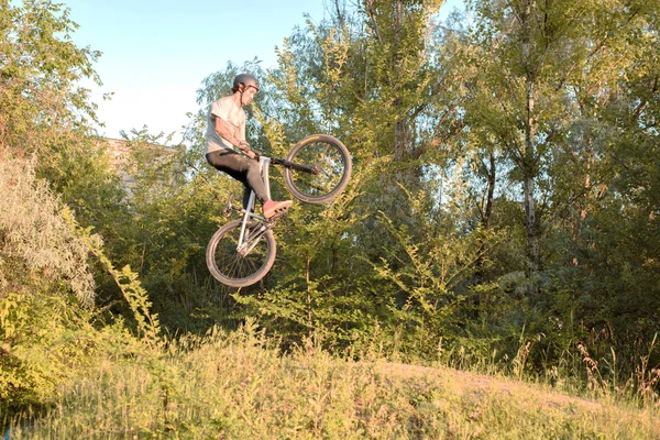 Młody kolarz skacze wysoko i robi sztuczki z rowerem. niezwykły kąt. w lesie przed zachodem słońca — Zdjęcie stockowe