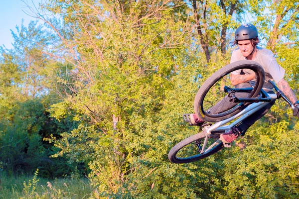 Jovem ciclista faz saltos e truques em uma bicicleta. na floresta contra o pôr do sol — Fotografia de Stock