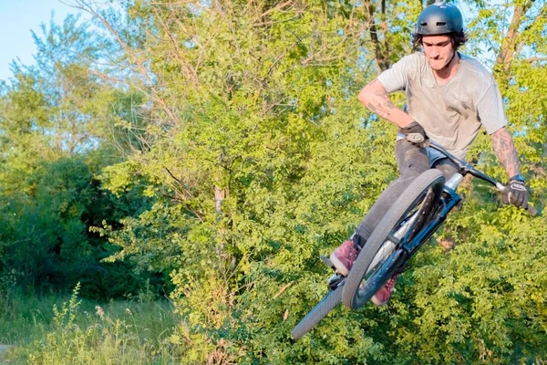 Jovem ciclista faz saltos e truques em uma bicicleta. na floresta contra o pôr do sol — Fotografia de Stock