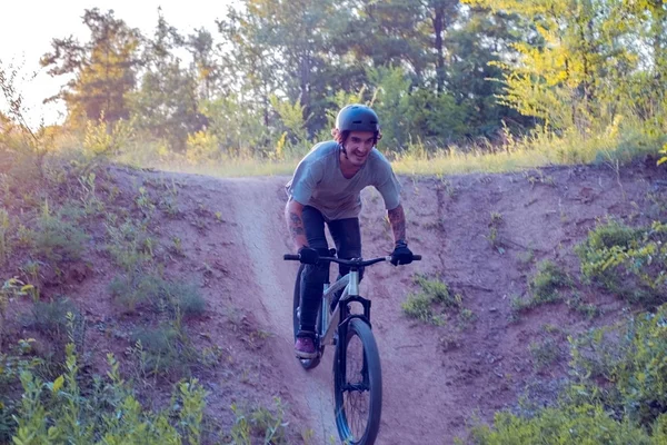 En ung kille, en cyklist med tatueringar, cykling. I skogen mot solnedgången — Stockfoto