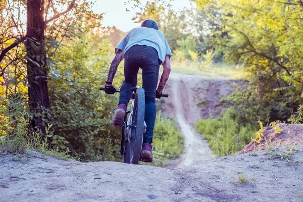 Um jovem, um ciclista com tatuagens, a andar de bicicleta. Na floresta contra o pôr-do-sol — Fotografia de Stock