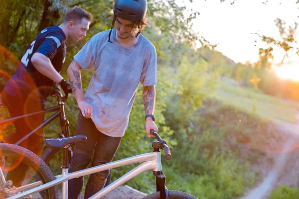 Dois ciclistas-amigos, com bicicletas, na floresta, contra o pôr do sol — Fotografia de Stock