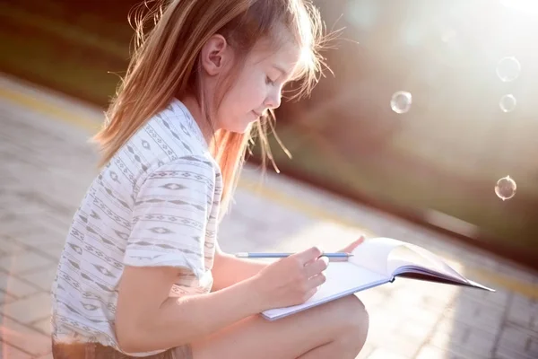 Retrato de uma linda menina sentada escrevendo em caderno. Estilo de vida exterior — Fotografia de Stock