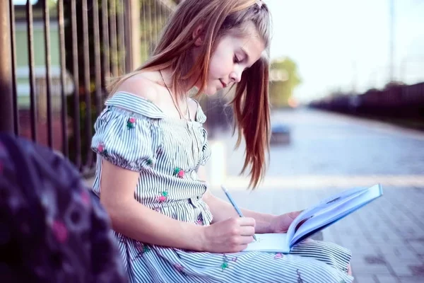 Retrato de uma linda adolescente com uma mochila. Sentado em um banco escrevendo em um caderno — Fotografia de Stock