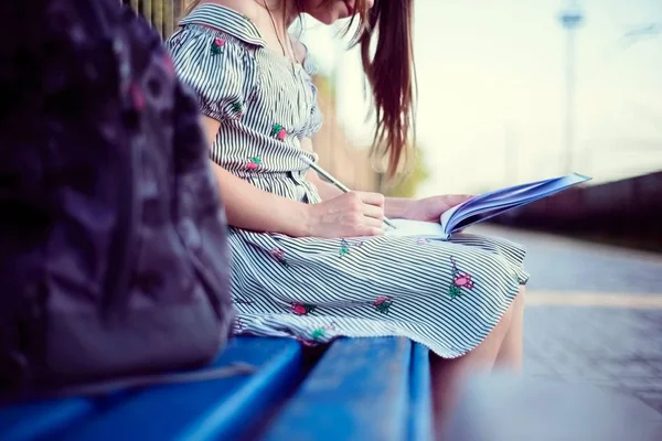 一个带着背包的漂亮少女的画像坐在写书的长椅上 — 图库照片