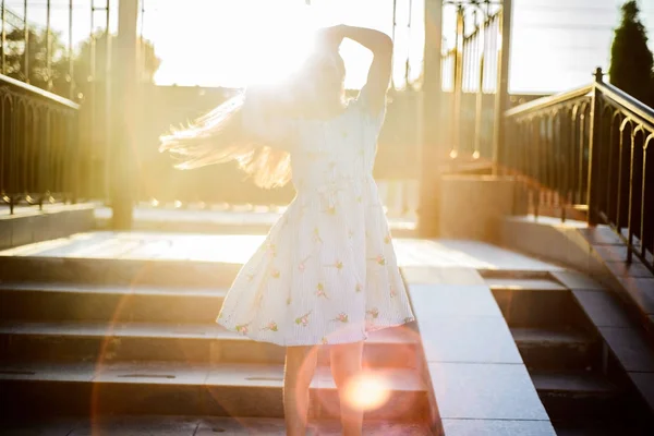 Porträtt av en vacker liten flicka, i en fashionabel klänning, uträtning håret på en solig sommardag, utomhus.Liten flicka med långt hår. Skönhet och mode baby med friskt hår — Stockfoto