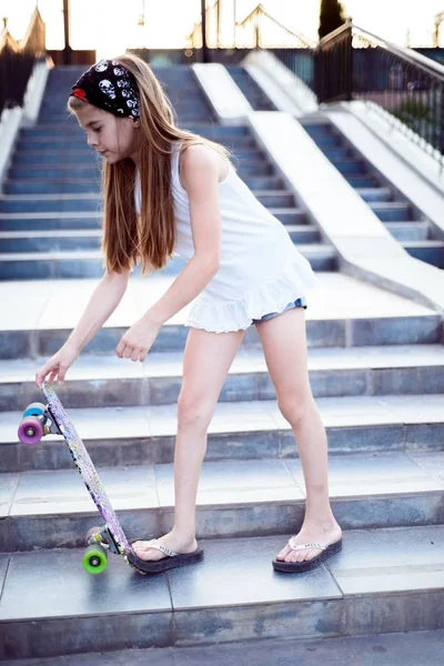 Menina bonita criança em uma bandana segurando um skate — Fotografia de Stock