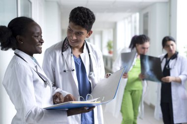 Bir grup melez doktor. Hastane koridorunda dikilen beyaz önlüklü gençler gülümsüyor ve ellerinde tıbbi belgeler tutuyorlar. Sağlık sorunlarını tartışın