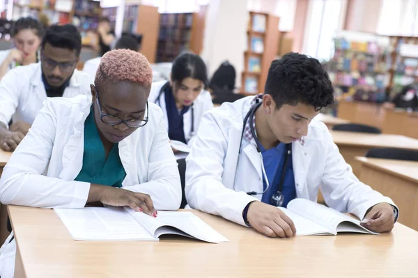 En grupp multietniska rasstudenter vid ett medicinskt universitet. Vi sitter vid bordet, vi skriver, vi läser, vi klarar provet — Stockfoto