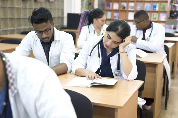 Skupina mladých multietnických ras, studentů medicíny. Čtěte učebnice, zatímco sedíte za stolem. Tupost zkoušek, studium — Stock fotografie