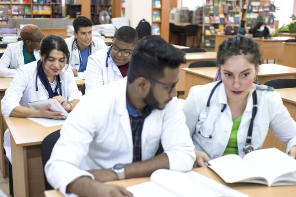 Багатонаціональна група студентів-медиків, які сидять за столом, вивчають медичну літературу — стокове фото
