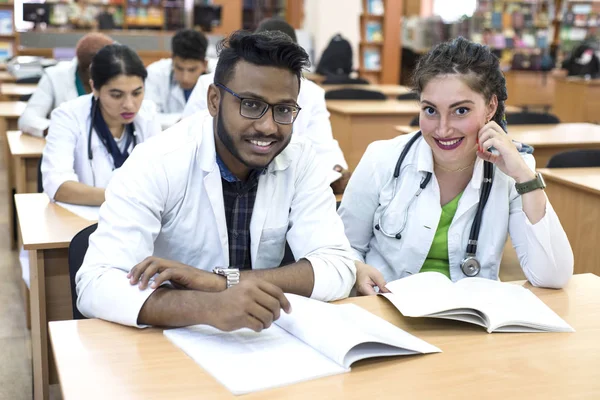 Een groep jonge geneeskundestudenten van gemengd ras. Zittend aan tafel, kijkend naar de camera, glimlachend — Stockfoto