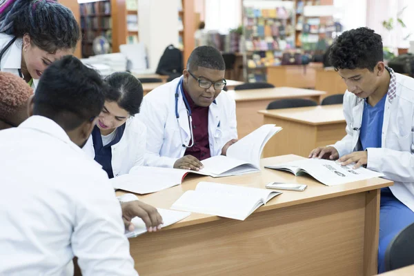 Un gruppo di giovani dottori, razza mista. Seduto al tavolo, i colleghi discutono argomenti medici — Foto Stock