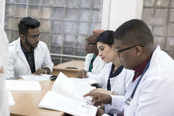 Doctor en medicina. Un grupo de jóvenes de raza mixta, sentados en una mesa en la oficina del hospital, leen literatura médica — Foto de Stock