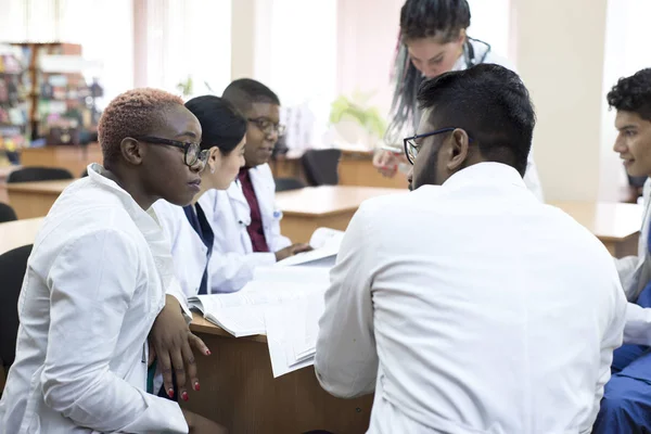 Doctor of medicine. A group of young people of mixed race, sitting at a table in the office of the hospital, read medical literature — 스톡 사진