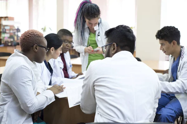 Doctor of medicine. A group of young people of mixed race, sitting at a table in the office of the hospital, read medical literature — 스톡 사진