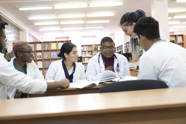 Молоді лікарі Люди змішаної раси, сидячи в білих халатах, в кабінеті лікарні, за столом, обговорюють медичні питання — стокове фото