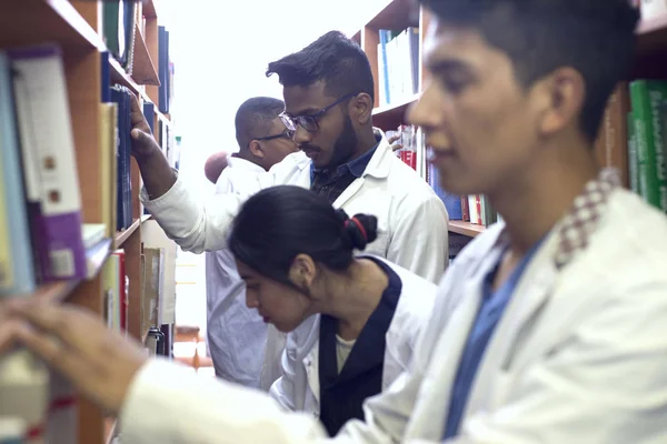 Grupa młodzieży, studenci medycyny, mieszana rasa. W bibliotece, między półkami, studiując literaturę medyczną. — Zdjęcie stockowe