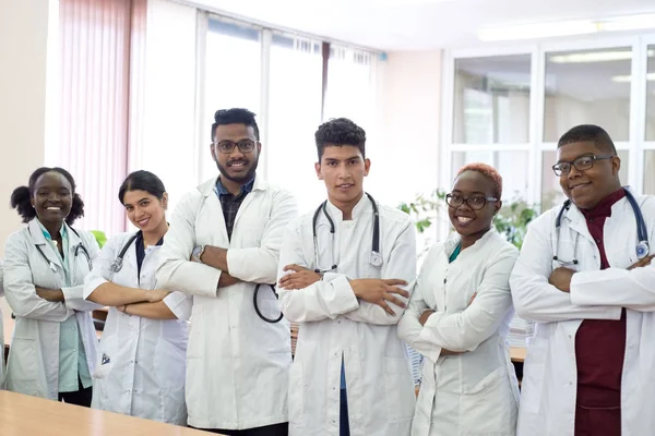 A group of doctors in the hospital corridor. Team of mixed race young men in white coats, with phonendoscopes, smiling — 스톡 사진