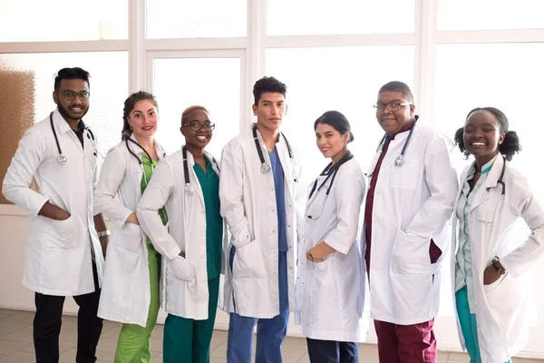 Team of young doctors, mixed race. People of different sex, in white coats, with phonendoscopes, posing, smiling — Stok fotoğraf